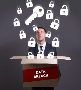 A man in a suit holding a cardboard box that is labelled 'data breach'. The lid of the box is open and there are white key and padlock symbols coming out of the box. The man is looking at the symbols with a shocked expression. 