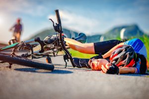 A cyclist laying down on the road holding their bleeding knee following an accident.