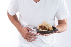 A man with a dumpling in his hand on a black tray. He has his other hand over his stomach as if in pain.