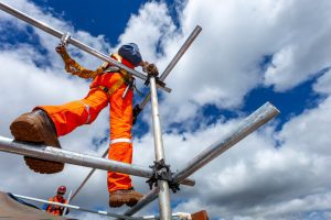 A construction worker in orange high-vis trousers walks across scaffolding