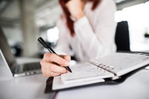 A woman sits at a desk taking notes. 