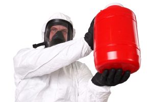 A man in a bio hazard suit holding a red bottle of hazardous material.