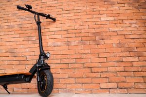 An electric scooter leaning against a brick wall. 