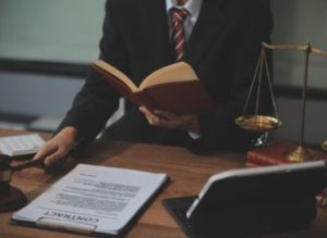 A psychological injury claim solicitor reading a book while sat at a desk which has a contract agreement form on it. He is an expert in PTSD compensation payouts.