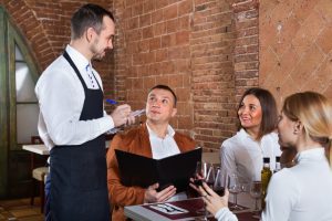 WAITER TAKING ORDER FROM A GROUP OF GUETSS IN A RESTAURANT