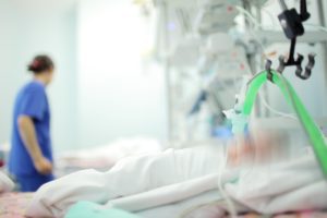 A nurse is shown in the background next to a baby in hospital. 