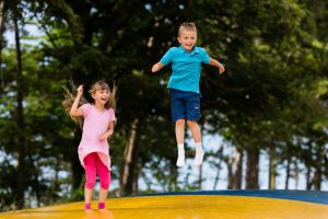 TWO CHILDREN BOUNCING ON A TRAMPOLINE IN A PLAYGROUND