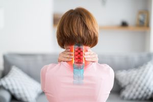 A woman holds her neck. A herniated disc injury is highlighted. 