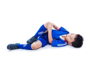 An injured child in a blue football uniform holding his knee. 