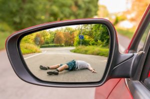 A pedestrian hit by a car and visible in the rear view mirror of car.