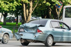 The back of a blue car completely trashed after being in a rear-end traffic accident with an uninsured driver.