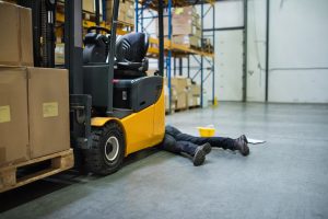 A warehouse worker laying on the ground after a forklift truck accident