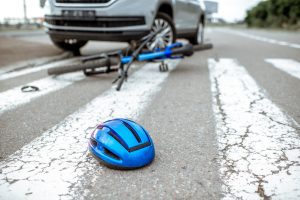 Blue bike under the wheel of a silver car after the car has hit a cyclist. The cyclist can start a bicycle accident claim.