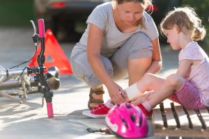 A woman bandages her child's ankle after a bicycle accident. The child's bike is discarded on the ground. The woman can start a bicycle accident claim on behalf of her child