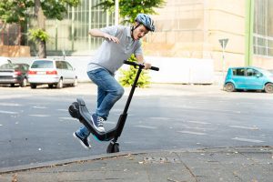 A young man riding an e scooter, crashing into a curb causing him to fall off