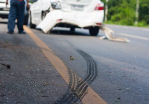 A damaged white car on the road with tyre marks. 