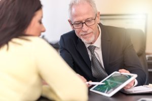 A solicitor helps their client with their No Win No Fee claim. They sit at a desk and look at a table and look at a tablet