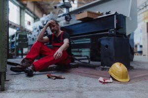 INJURED WORKER SITTING ON FLOOR NEXT TO FAULTY MACHINERY