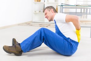 A man in blue overalls sits on the floor after suffering a back injury at work