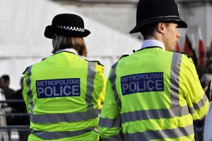 Two Metropolitan Police officers stand together in hi-vis jackets.